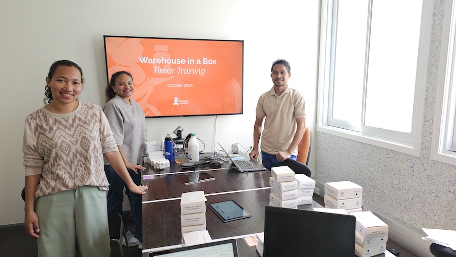 Leticia, Bernadette, and Estaquio from the Timor Team standing in front of a screen that says "Warehouse in a Box, Timor Training, October 2024"